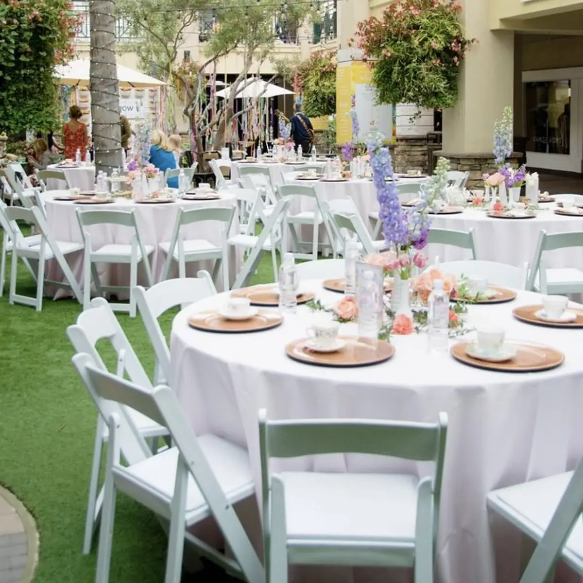 Round tables and white resin folding chairs set up for an outdoor courtyard event