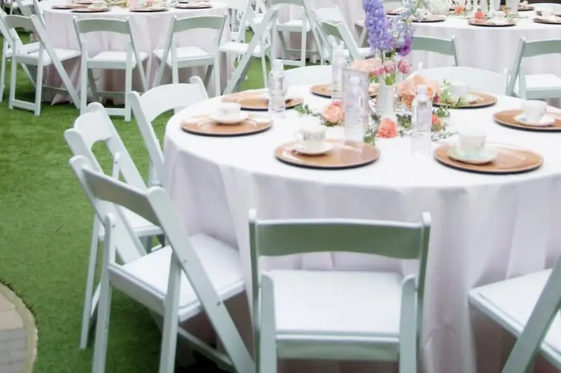 Round tables and white resin folding chairs set up for an outdoor courtyard event