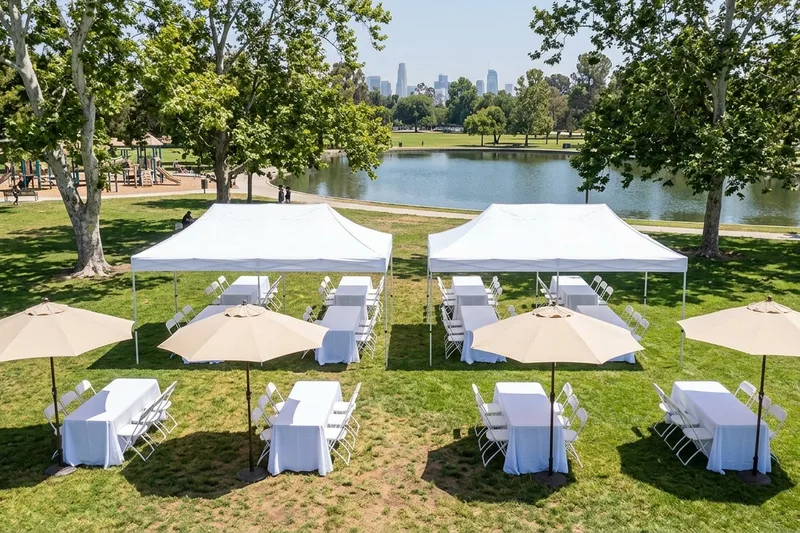 Community event in a park with white canopies, rectangle tables, white folding chairs and canvas market umbrellas